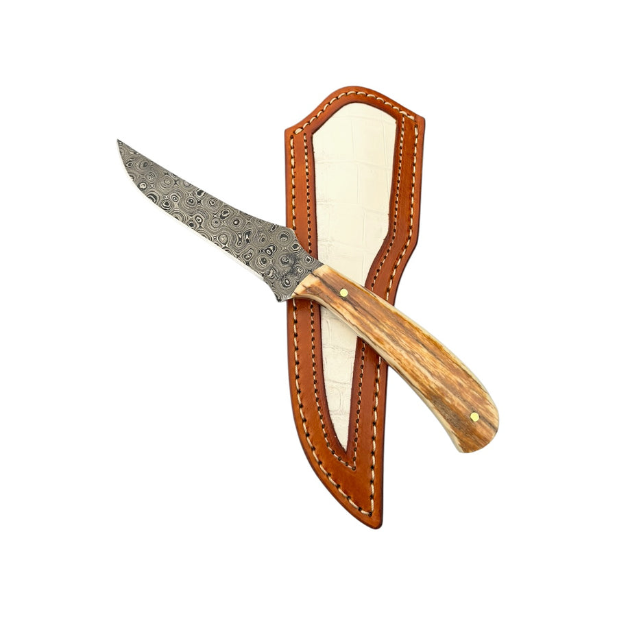 Damascus mammoth skinning knife 26-558 resting across a brown stitched sheath with a cream-colored inset.