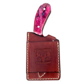 A handcrafted knife with a vibrant pink and purple handle, partially pulled from its brown leather sheath.